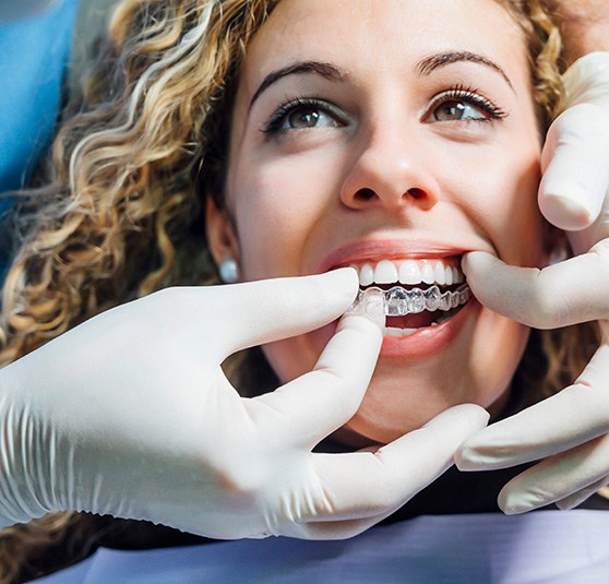 Dentist inserting Invisalign aligner into female patient’s mouth