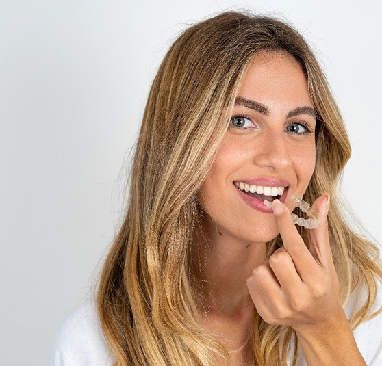 Young woman smiling while holding Invisalign aligner